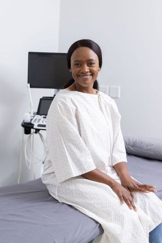 Smiling african american woman sitting on exam bed in gown beside ultrasound monitor