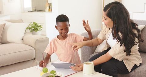 Woman guiding boy using tablet for learning and play in cozy living room