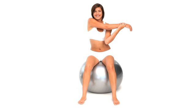 Woman stretching while seated on a silver gym ball. This video highlights an energetic and positive attitude towards fitness and exercise. Ideal for promotional materials for gyms, fitness products, health blogs, exercise tutorials, and wellness programs.