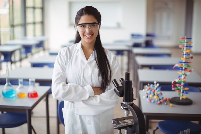 Schoolgirl in lab coat standing with arms crossed in a science classroom, smiling confidently. Ideal for educational materials, science and STEM promotion, school brochures, and academic websites.