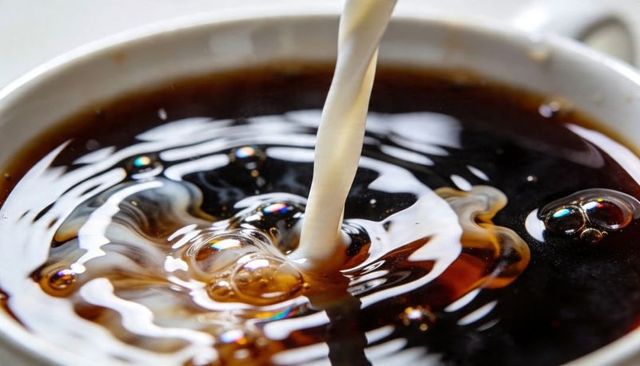 Pouring milk into black coffee creating swirling cream bubbles and liquid ripples macro