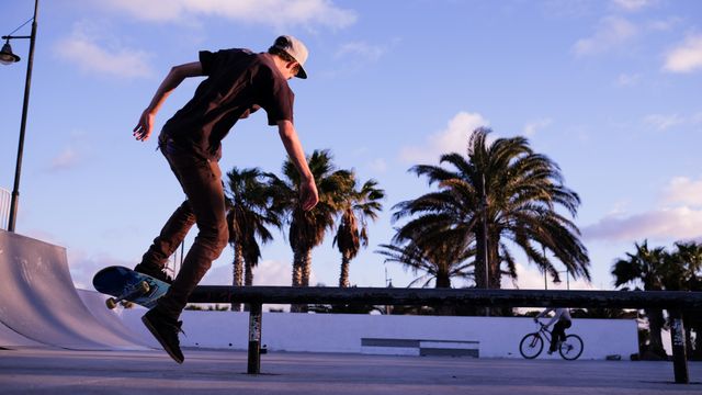 Teen executing a skateboard trick at an outdoor park against a backdrop of palm trees and a vibrant sunset. This captures the vibrant and energetic essence of youth culture and urban sports. Perfect for use in articles, advertisements, or promotions focused on active lifestyles, skating communities, travel, and outdoor activities.