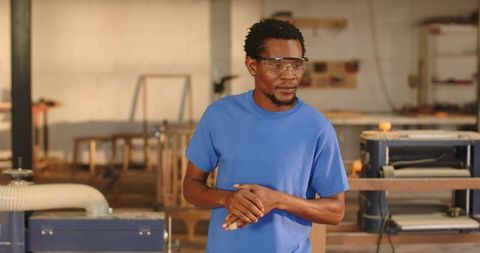 Craftsman wearing safety goggles in woodshop full of tools and machinery