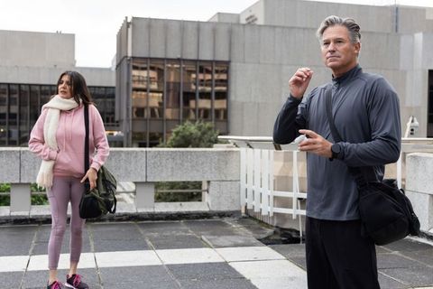 Middle-aged duo preparing for rooftop workout in city, man adjusting earbud