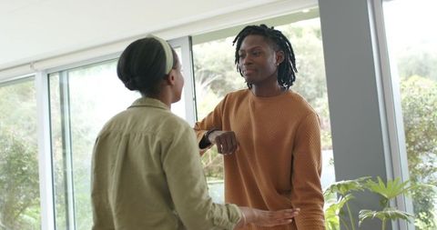 African American couple exchanging elbow greeting in modern living room with large windows