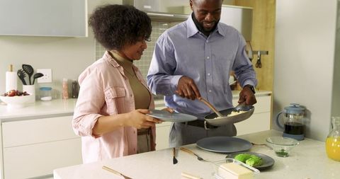 Black couple preparing breakfast together in modern kitchen serving scrambled eggs