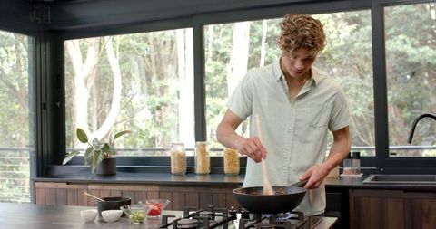 Young Man Cooking Stir-Fry in Modern Kitchen Interior