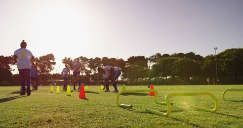 Female soccer team training on grass club pitch at sunset with cones, hurdles and drills