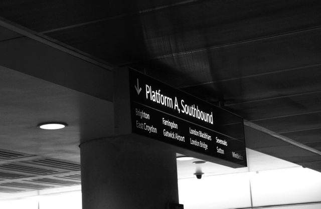 This black and white photo shows a sign for the southbound platform at a modern urban train station. Destinations listed include major cities and airports, suggesting a hub of activity. Could be used for articles on travel, urban infrastructure, train station design, or transportation guides.