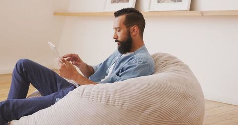 Man relaxing on beanbag using digital tablet at home