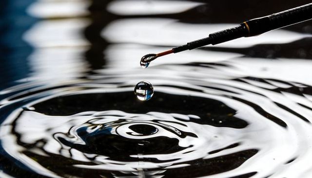 Fishing rod tip dripping water droplet hovering over high-contrast rippling surface