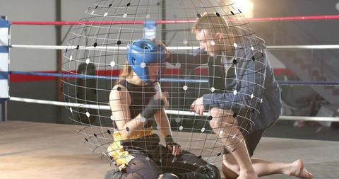 Woman boxer resting while coach adjusting headgear in ring with digital grid overlay