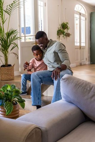 African american father and son sitting on steps sharing tender moment in sunlit living room