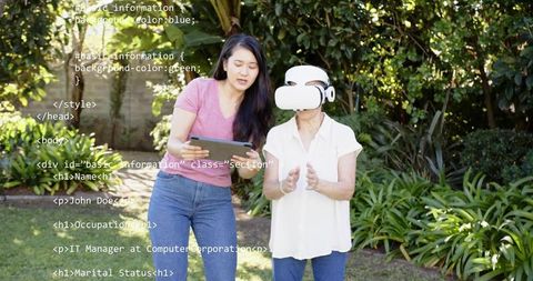 Caregiver guiding senior using vr headset in garden with tablet and code overlay