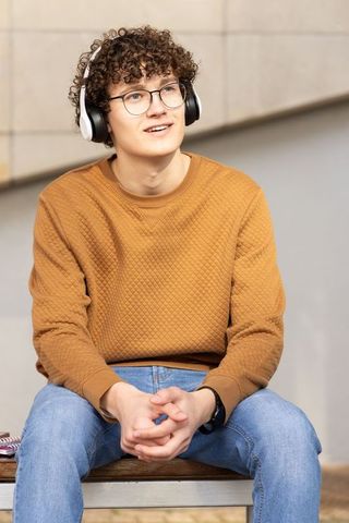 Teen listening to music on urban bench wearing glasses and mustard quilted sweatshirt