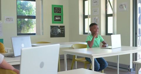 African American teen using laptop in bright classroom smiling while learning