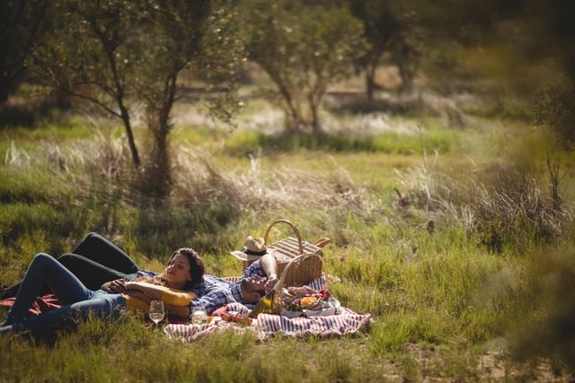 Young couple enjoying a peaceful day outdoors, lying on a picnic blanket at an olive farm. Ideal for themes of romance, relaxation, nature, and leisure activities. Perfect for use in lifestyle blogs, travel websites, and advertisements promoting outdoor activities and romantic getaways.
