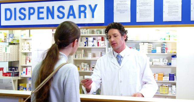 Pharmacist in white coat helping female customer with medication inside a well-organized pharmacy dispensary. Suitable for illustrating customer service in healthcare settings, pharmaceutical care, healthcare assistance, and professional interactions in medical environments.