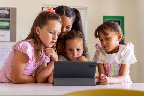 Elementary girls collaborating around tablet in classroom, focused digital learning