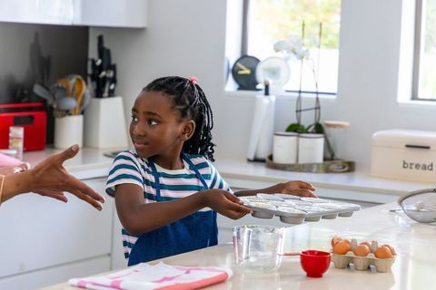 African american girl baking muffins in bright modern kitchen holding muffin tray smiling