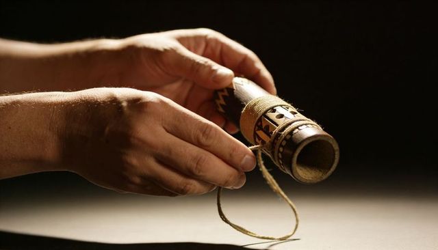 Artisan tying twine around carved wooden tube with geometric patterns