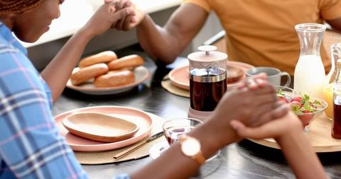 Family Holding Hands in Prayer Before Meal Around Dining Table