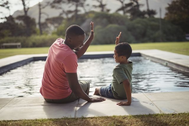 Smiling father and son giving high five to each other near poolside