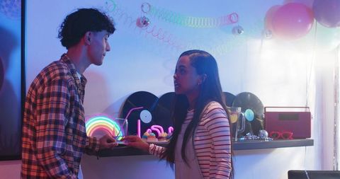 Diverse young couple exploring vinyl records and neon decor at retro house party
