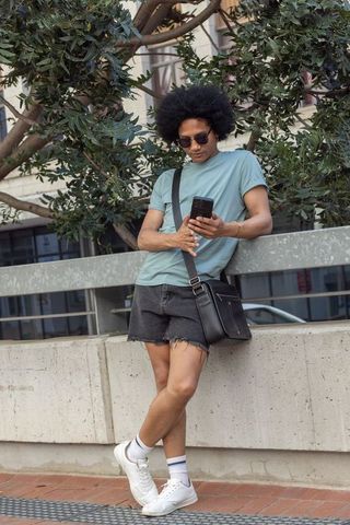 African american man leaning on city railing checking smartphone wearing sunglasses casual