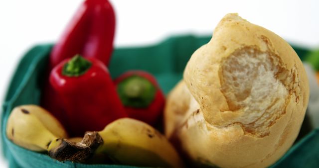 Close-up of assortment of fresh food items including a bread roll, red bell peppers, and bananas placed in a green basket. Useful for healthy eating concepts, grocery shopping themes, or food market advertisements.