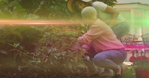 Two women tending flowering shrub in backyard with potted red blooms and patio chairs