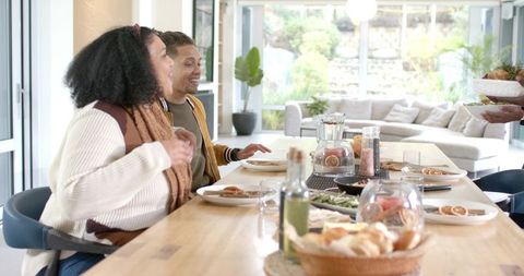 Couple sharing sunlit brunch at open-plan kitchen table, passing bowl and smiling
