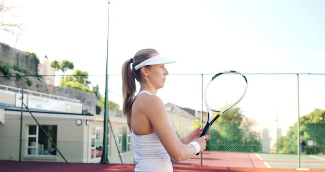 Female tennis player holding racket and wearing white athletic attire practicing on outdoor court. Ideal use for fitness promotions, sportswear advertisements, female empowerment campaigns, and sports training guides.