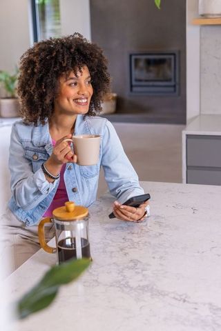 African american woman enjoying coffee while checking phone at bright modern kitchen island