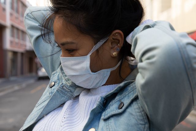 Close up of biracial woman out and about in the city during the day, standing in the street and putting on a face mask for protection against coronavirus covid 19