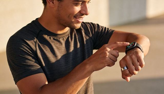 Smiling man tapping smartwatch during outdoor workout at golden hour