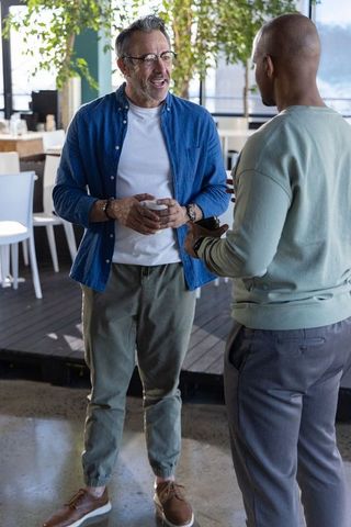 Senior professional chatting with colleague over coffee in modern sunlit office lounge