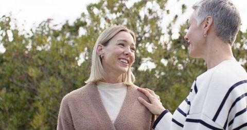 Two women chatting and smiling in garden, friend comforting friend, candid outdoor moment