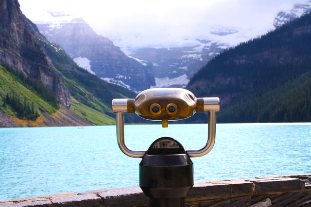 Binocular viewer focused towards tranquil mountain lake with foggy, snowy peaks rising in the background. valuable for travel articles, outdoor adventure promotions, nature appreciation campaigns, and landscape photography enthusiasts. ideal image for promoting serene travel destinations and adventure tours.