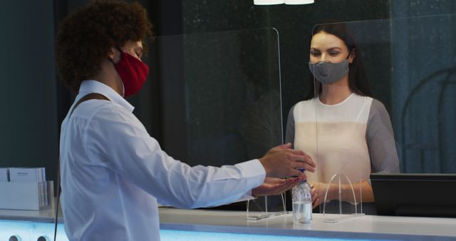 Biracial man and female receptionist wearing face masks at hotel reception desk. out and about during coronavirus covid 19 pandemic.