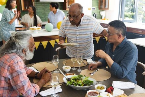 Senior indian man serving plate at multigenerational family dinner in modern kitchen