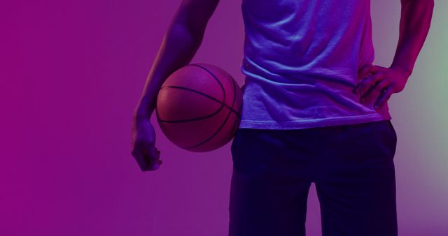 Image of low section of biracial male basketball player with ball on purple to green background. Sports and competition concept.