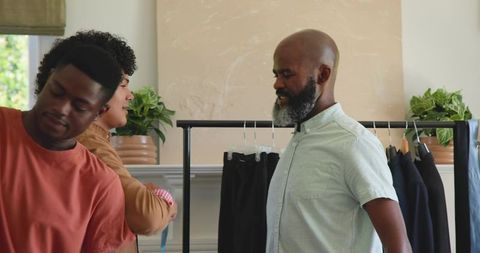 Mature man evaluating pants and coats on clothing rack in showroom with team