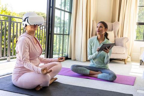 Practicing vr-guided meditation with instructor on yoga mats by sunlit balcony