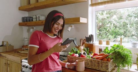 Smiling Woman Checks Smartphone with Organic Vegetables in Rustic Kitchen