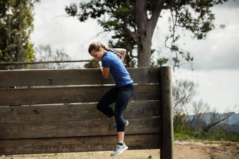 Young woman overcoming wooden obstacle in outdoors challenge