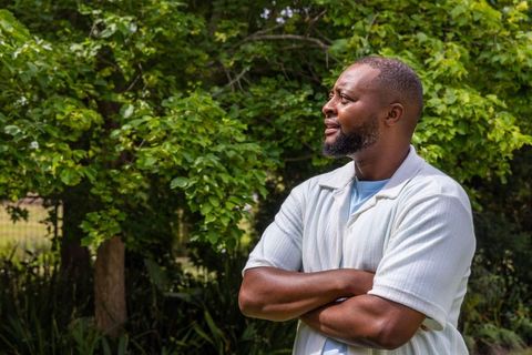 Confident african american man standing arms crossed looking thoughtful in sunlit garden
