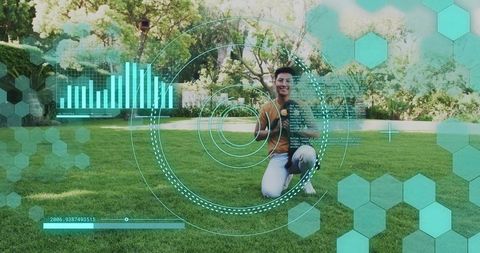 Kneeling Asian man giving thumbs-up on park lawn with futuristic digital HUD overlay