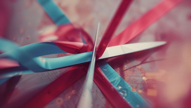 Scissors cutting red and blue ribbon on wooden surface