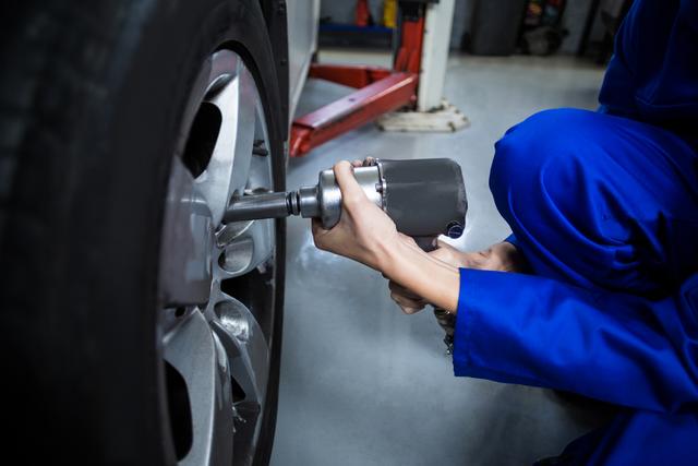 Hands of female mechanic fixing a car wheel with pneumatic wrench in repair garage
